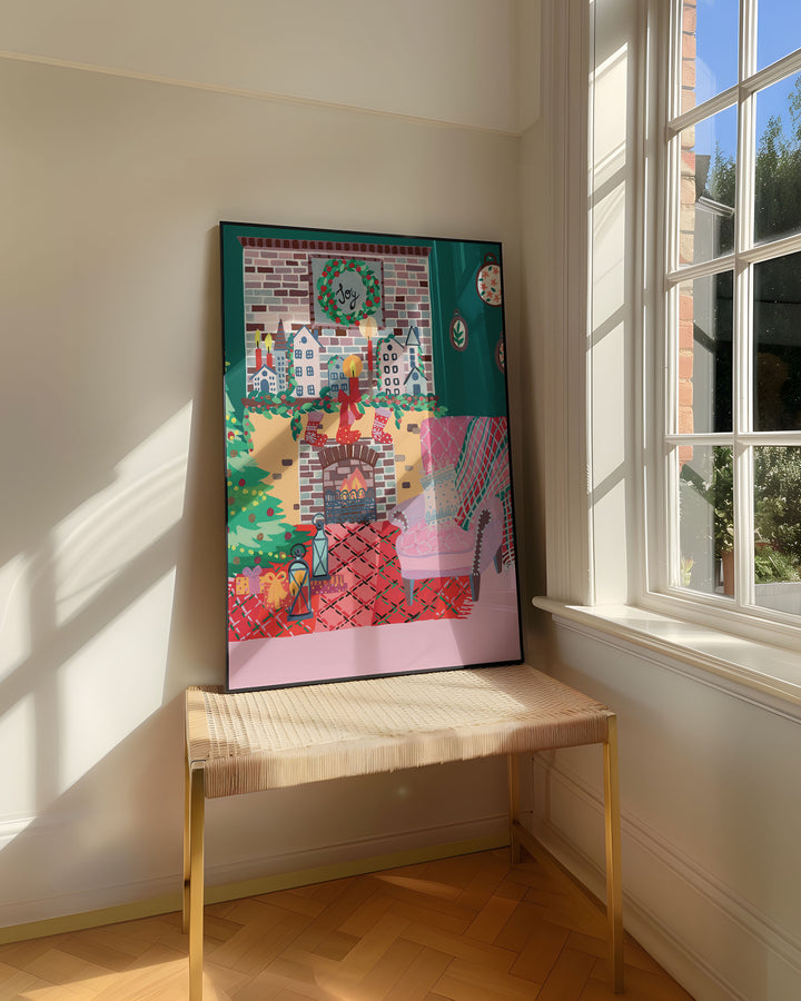 Framed Art Print titled 'Yuletide Haven' by Little Berries Studio, resting on a woven bench near a sunlit window in a bright, airy room.