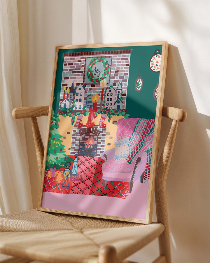 Framed Art Print titled 'Yuletide Haven' by Little Berries Studio, placed on a wooden chair in a softly lit room.